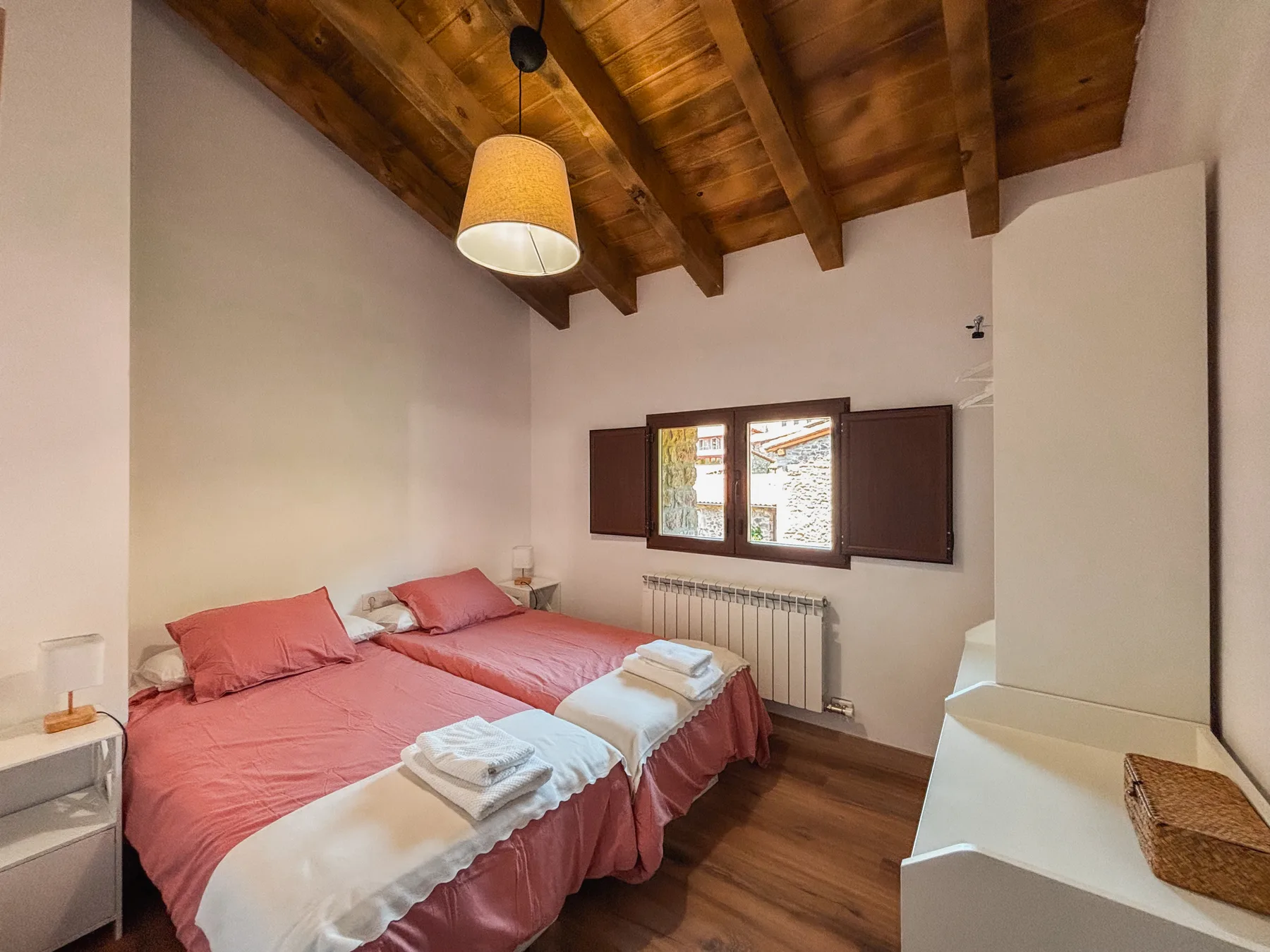 Dormitorio doble con vigas y ropa de cama rosa